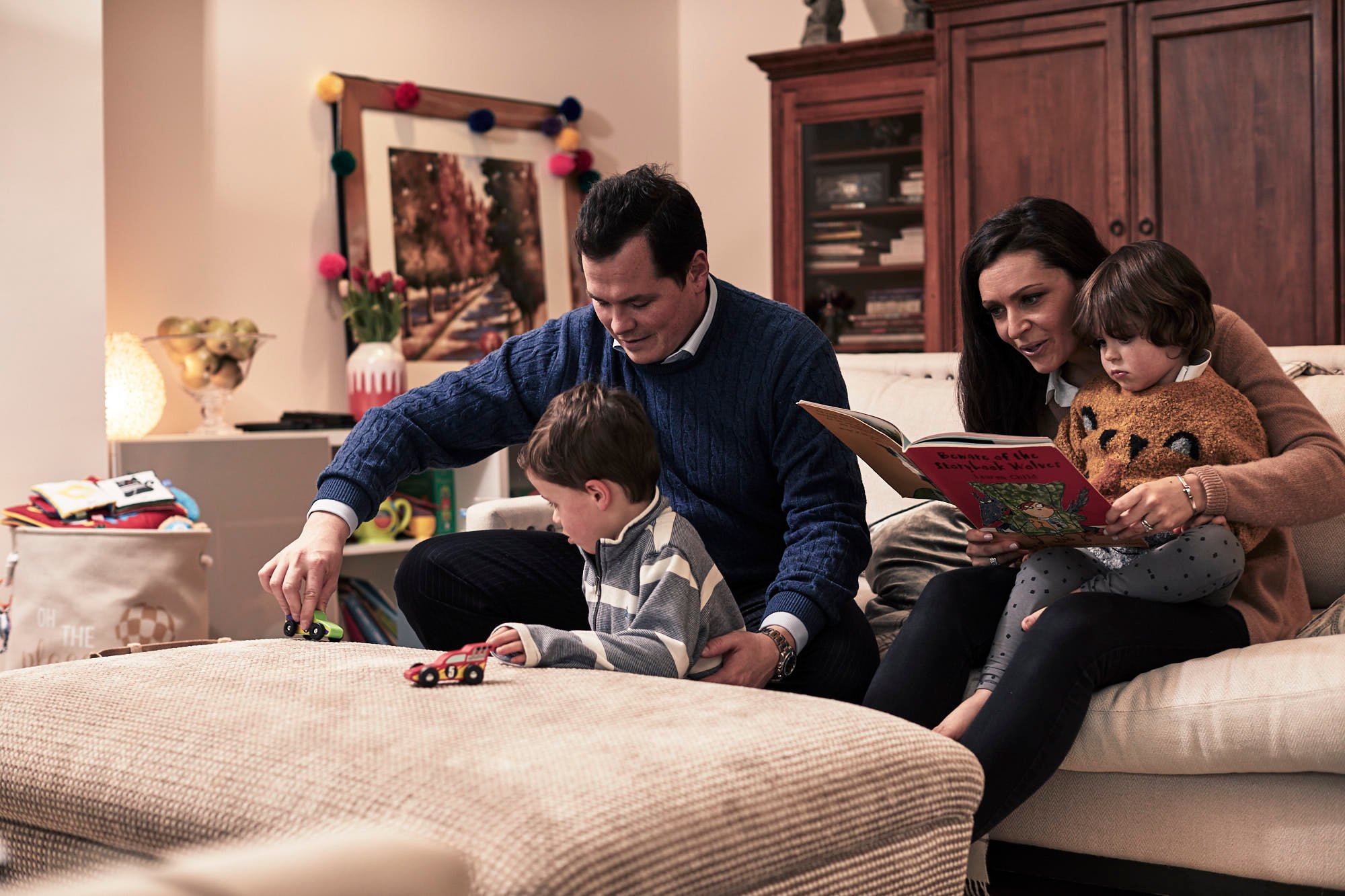 Family of Mum, Dad and two young boys sitting on sofa and reading stories