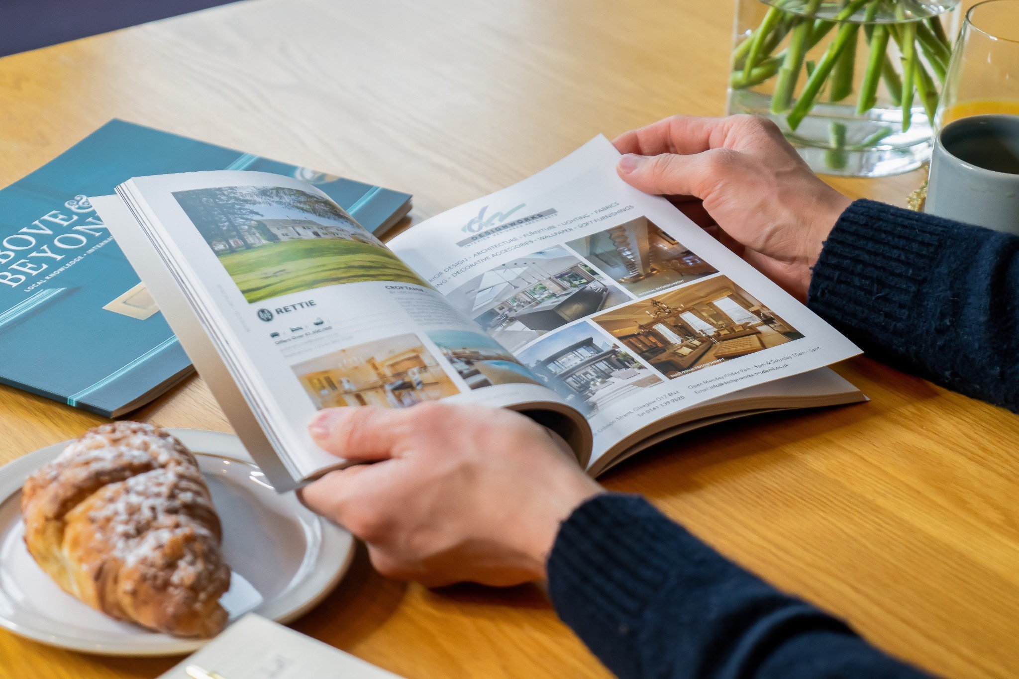 Photo of a persons hands with an open brochure and a croissant on the side