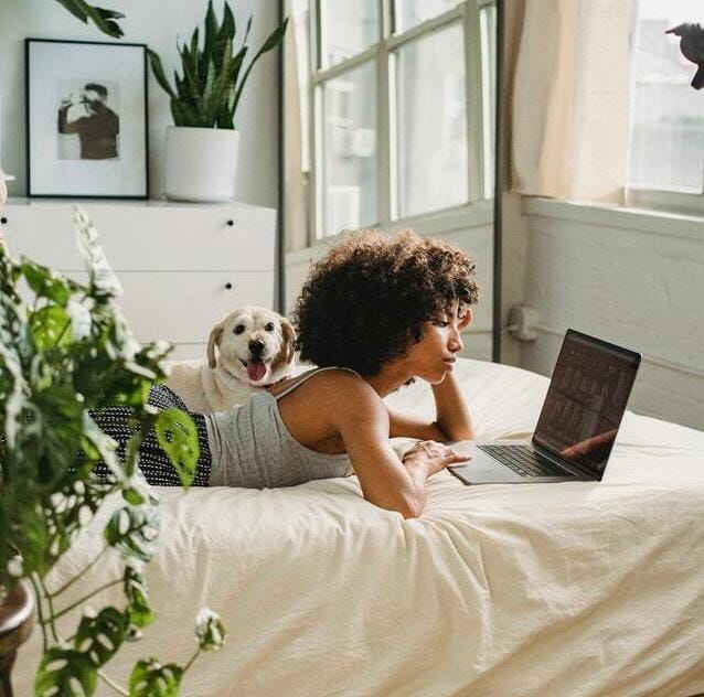girl with dog lying on bed looking at laptop